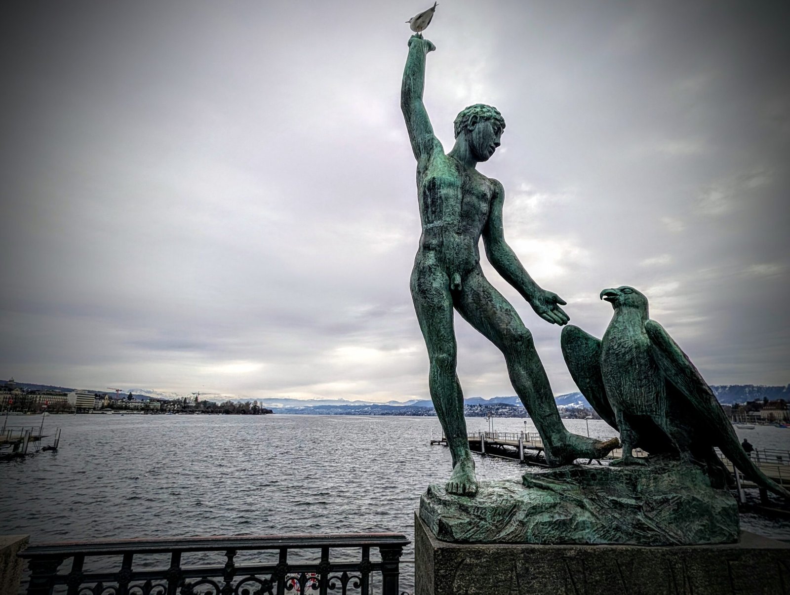 Bronze statue overlooking Lake Zurich with the Swiss Alps visible in the distance.