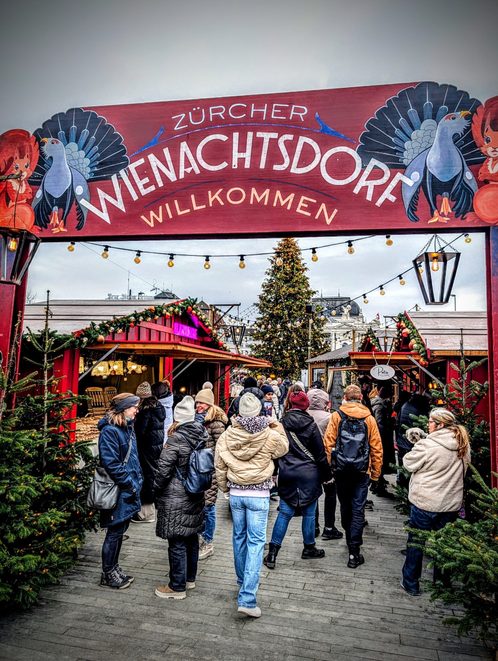 Crowds walking through the Zurich Christmas Market near the Zurich Opera House, with festive lights and holiday stalls.